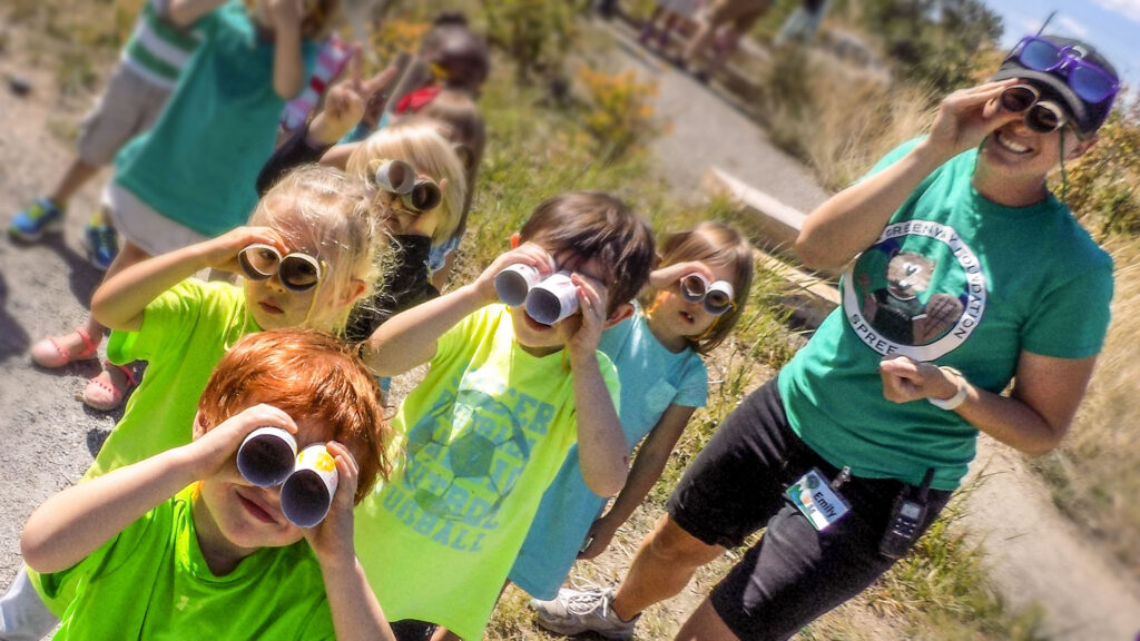 SPREE Preschool (ECE) Students on a field trip in Johnson Habitat Park hold crafty binoculars to their faces to focus on river ecology.