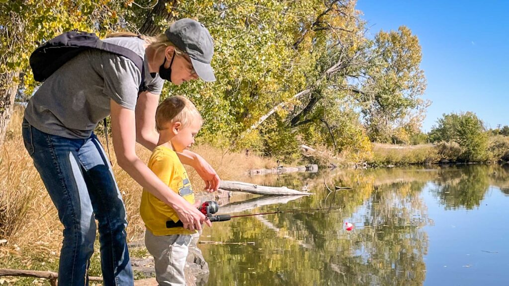 A parent helps their child learn to fish in Overland Pond at Family Fishing Day